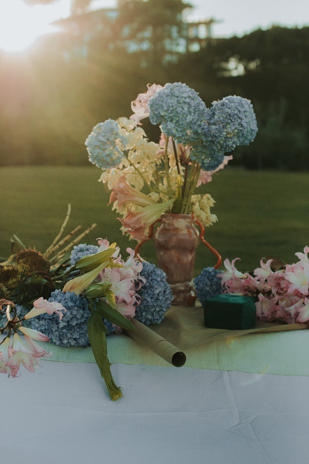 Outdoor tablescape styled with blue hydrangea, blush florals and dried elements around a terracotta vase