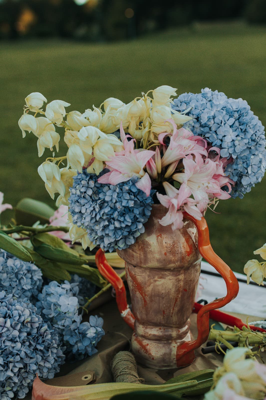 Detail of a terracotta vase filled with blue hydrangea and blush flowers, golden hour