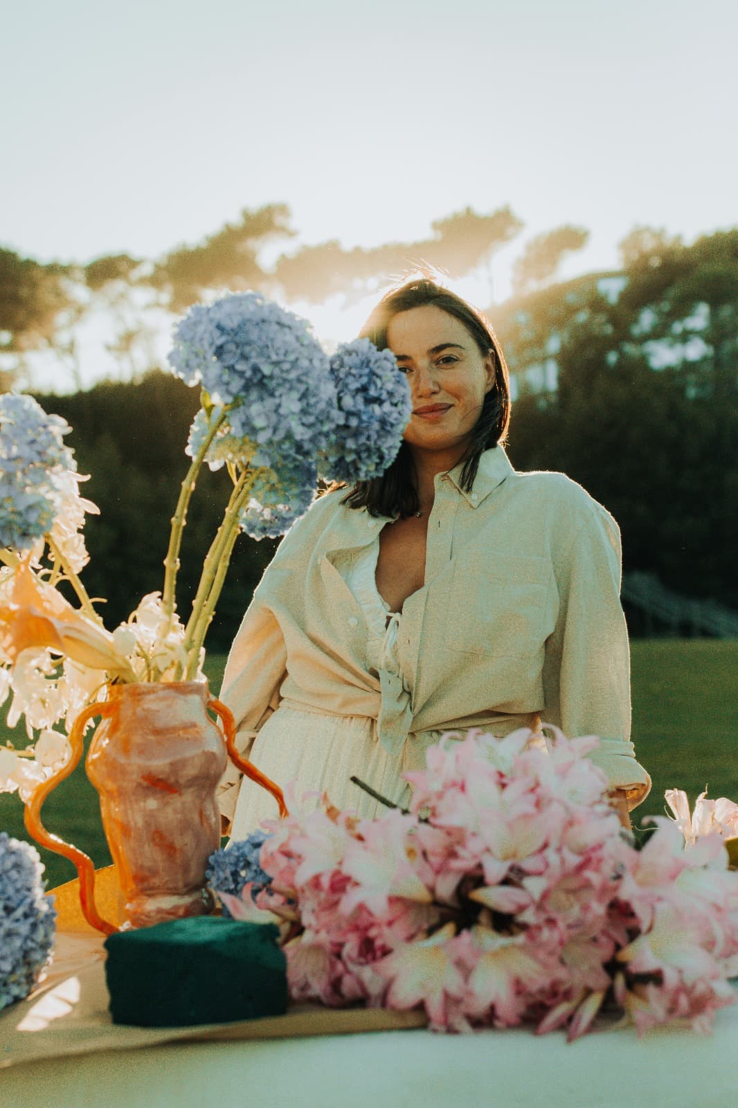 Person styling an outdoor event table with blue hydrangea and blush flowers, golden hour
