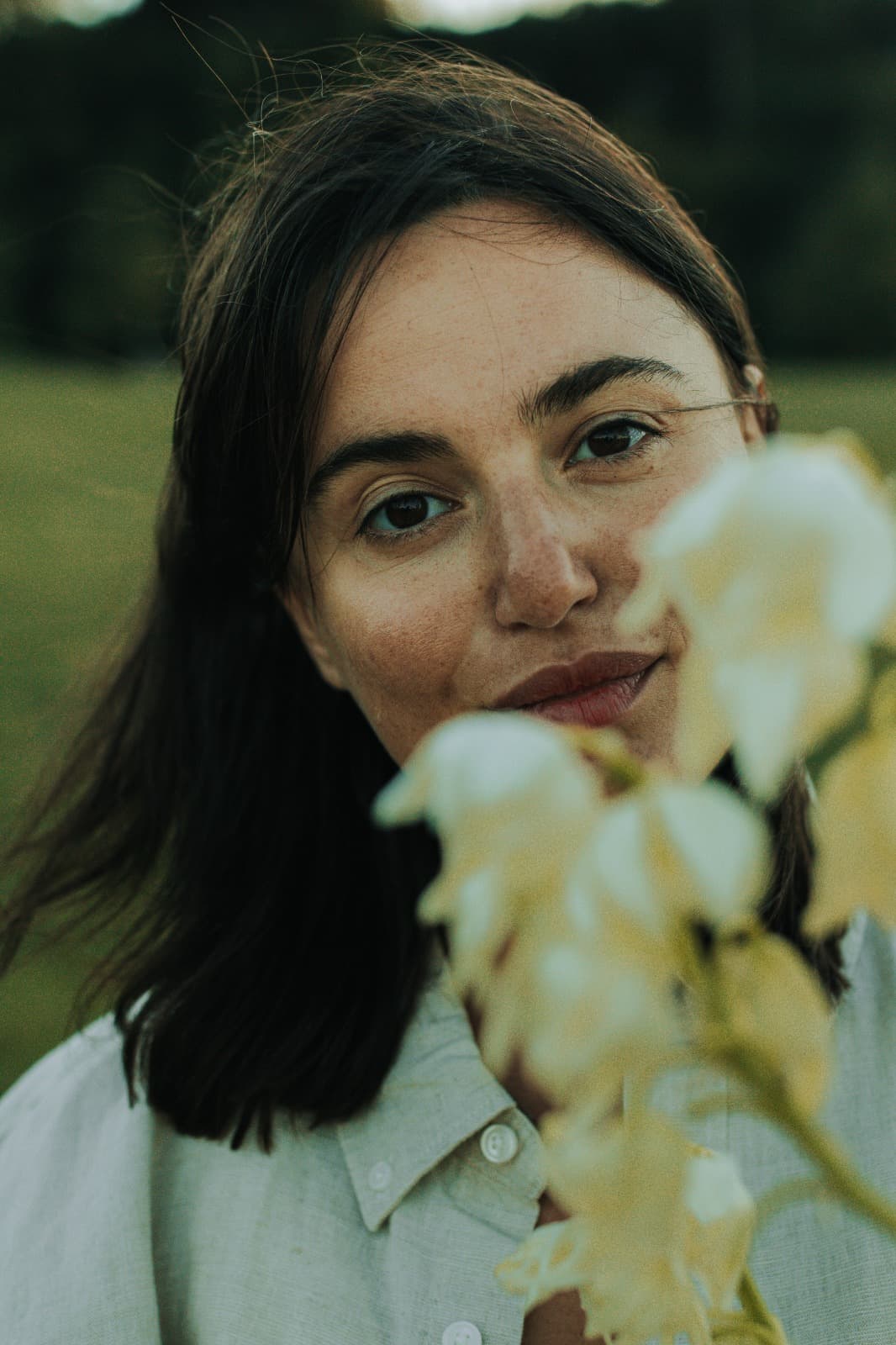 Close portrait of a person beside pale floral stems, softly lit outdoors